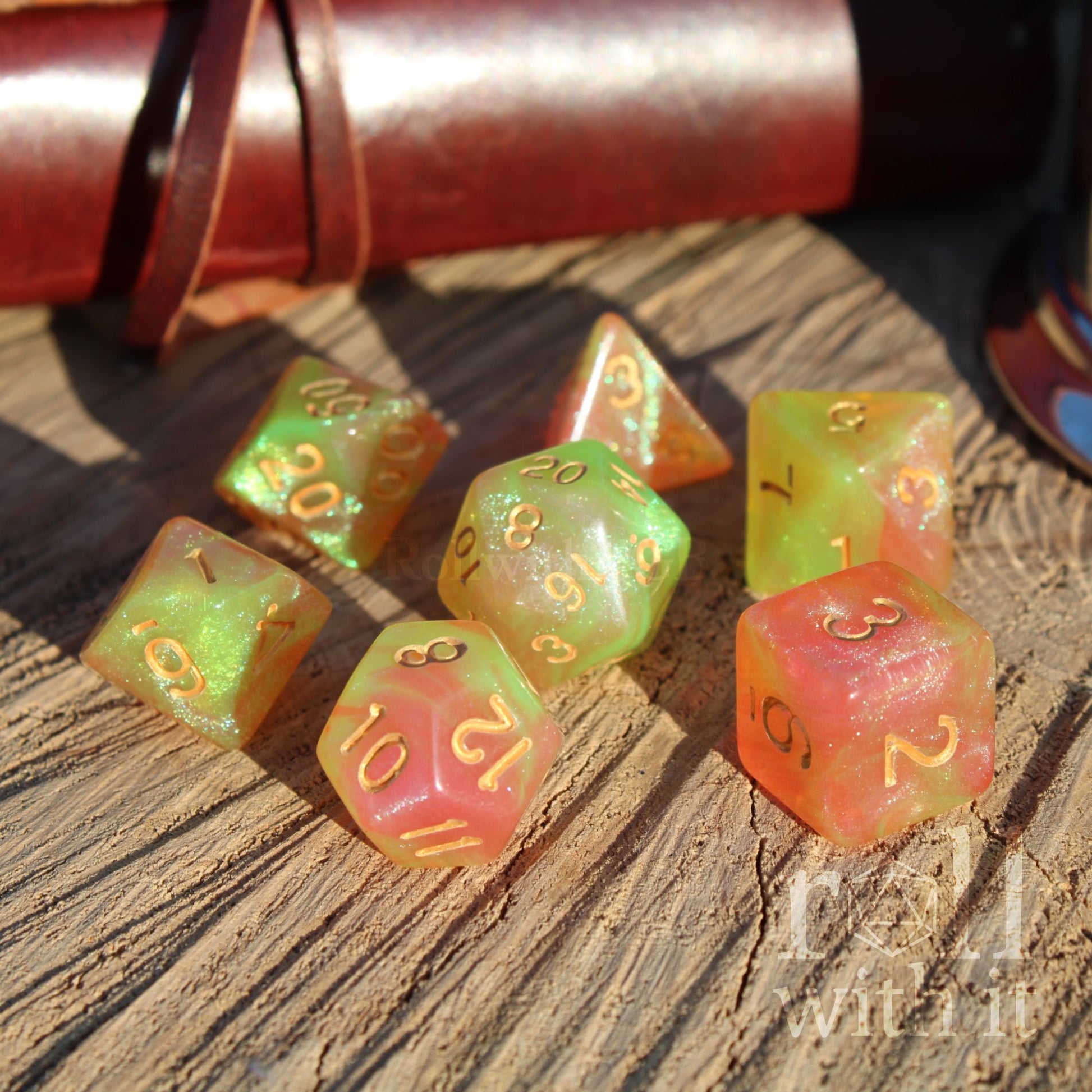 Set of colorful glitter filled spring green yellow and peach pink mxied polyhedral dice on a wooden surface with a leather-bound book in the background.