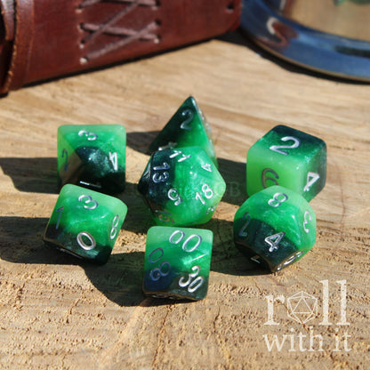 Set of 7 green layered dark black polyhedral dice set on a wooden surface with 'roll with it' branding.