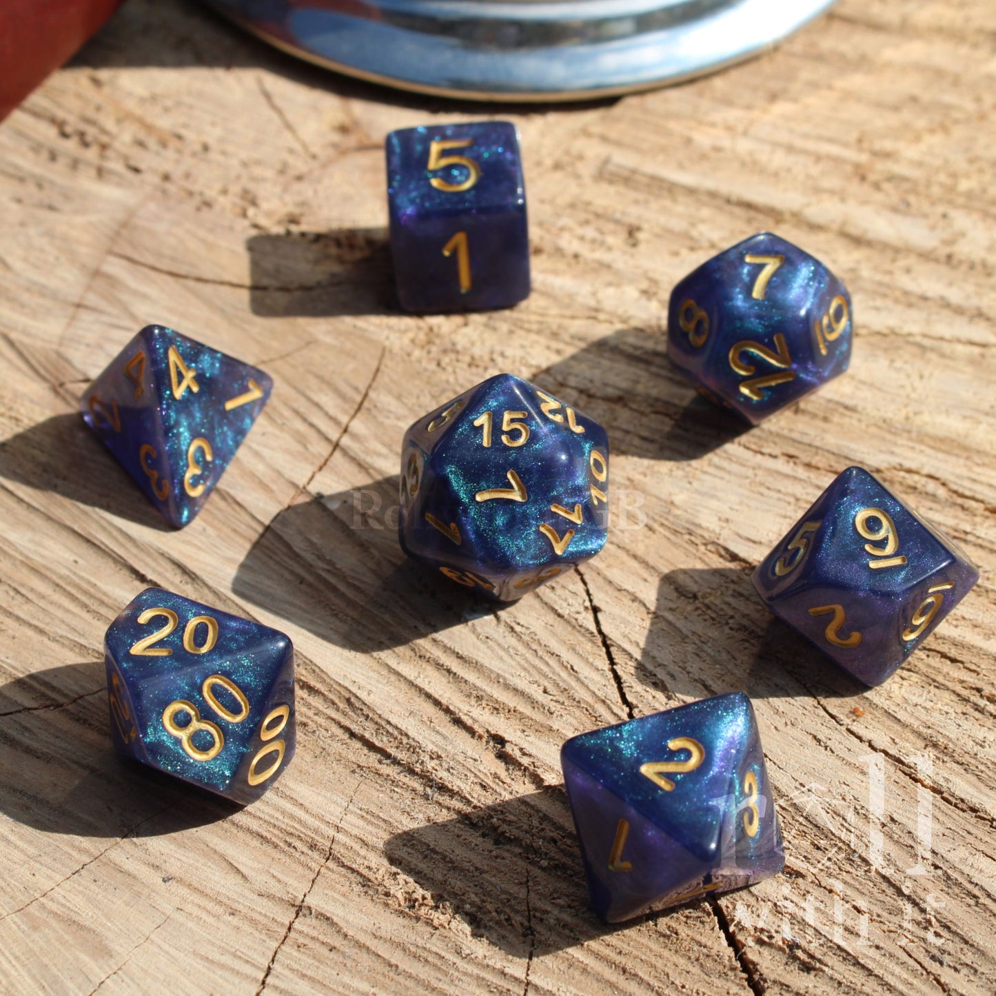 Set of 7 blue glitter filled star nebula aesthetic polyhedral dice with gold numbers on a wooden surface