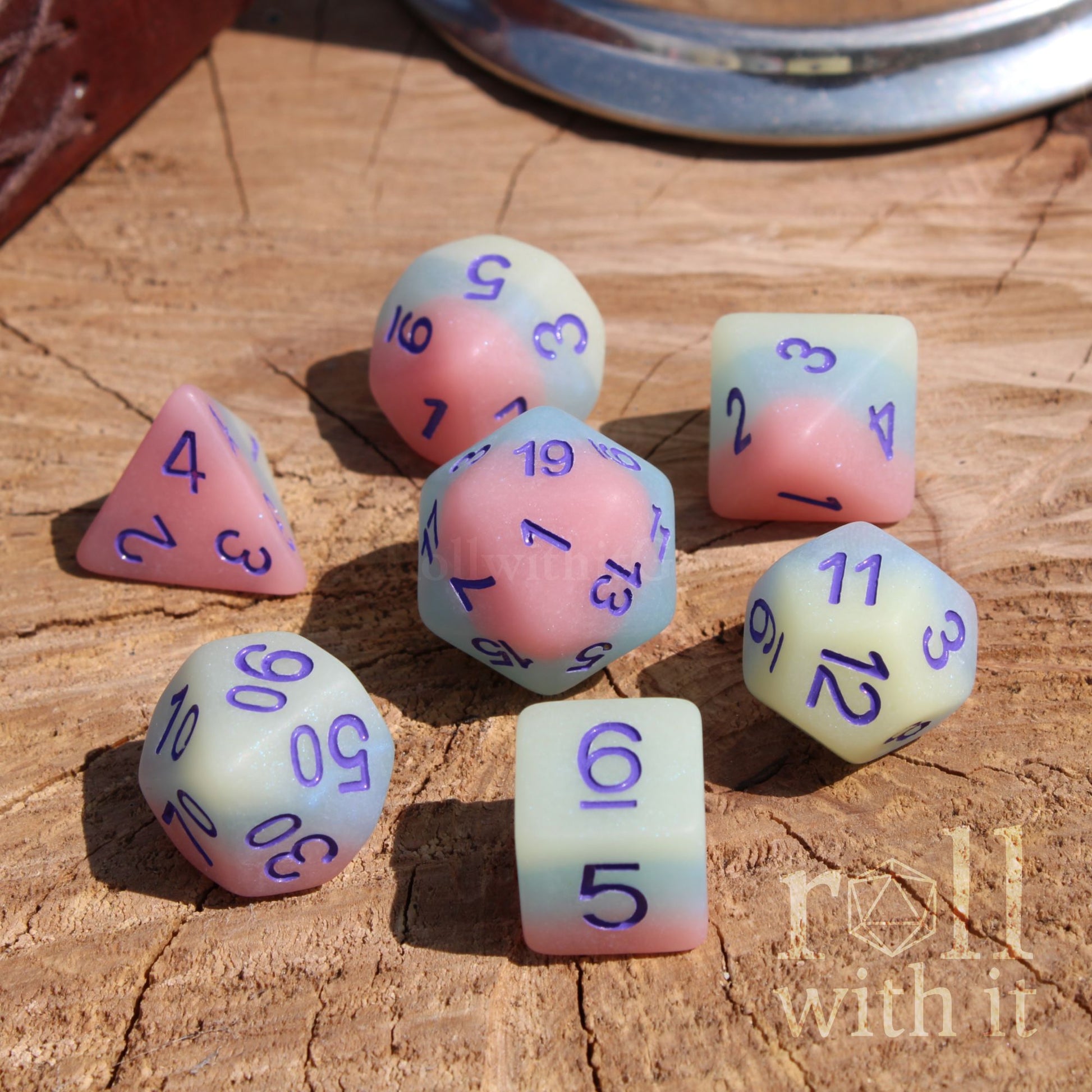 Set of colorful matte dungeons and dragons polyhedral dice with numbers on a wooden surface, featuring the brand 'roll with it'.