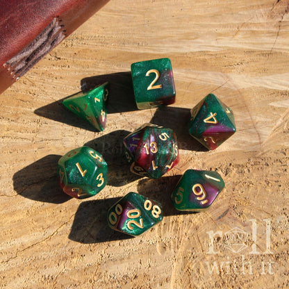 Set of polyhedral dice with dark swirling green and purple colors on a wooden surface, featuring the 'Roll With It' brand.