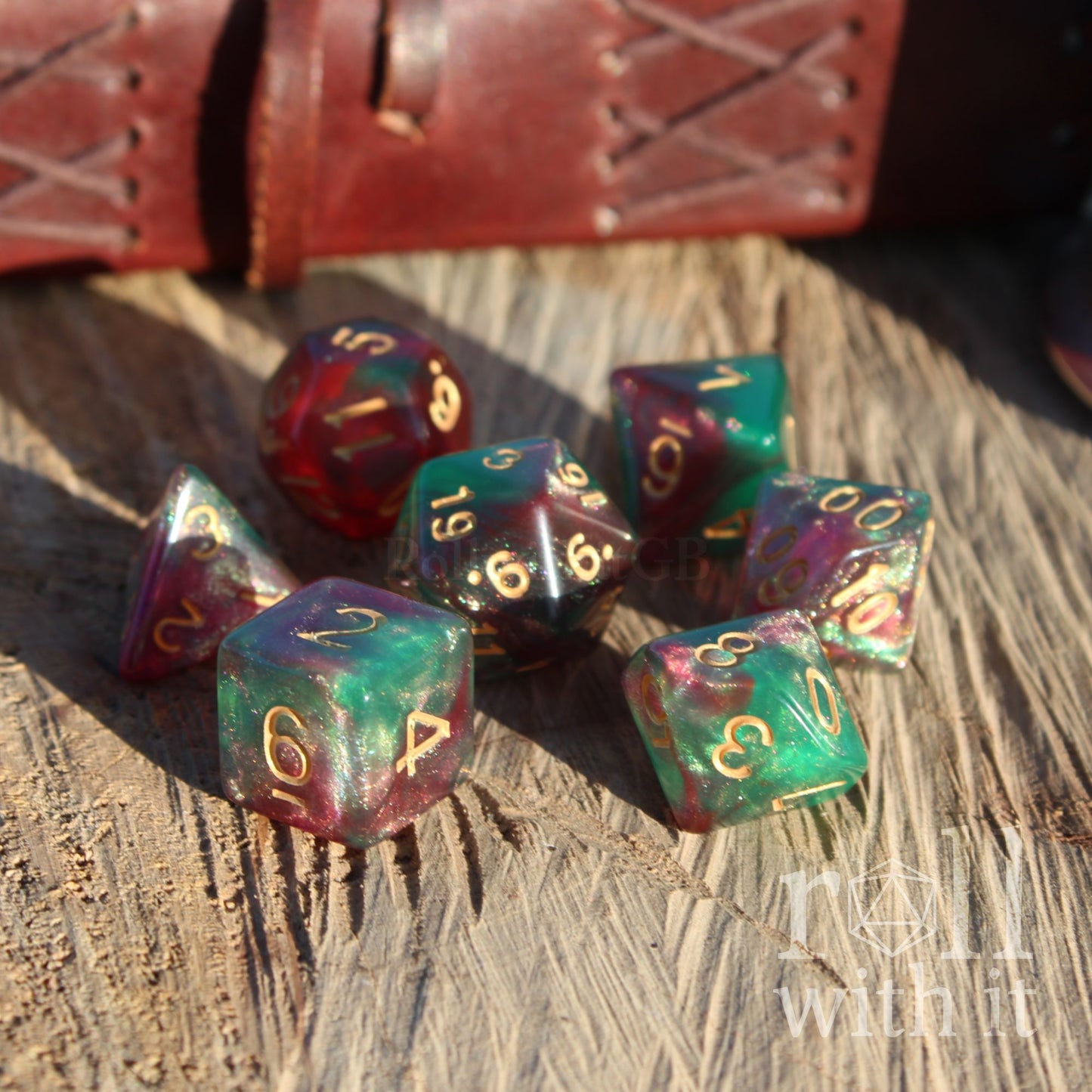 Set of colorful emerald green purple polyhedral dice on a wooden surface with a leather-bound book in the background.