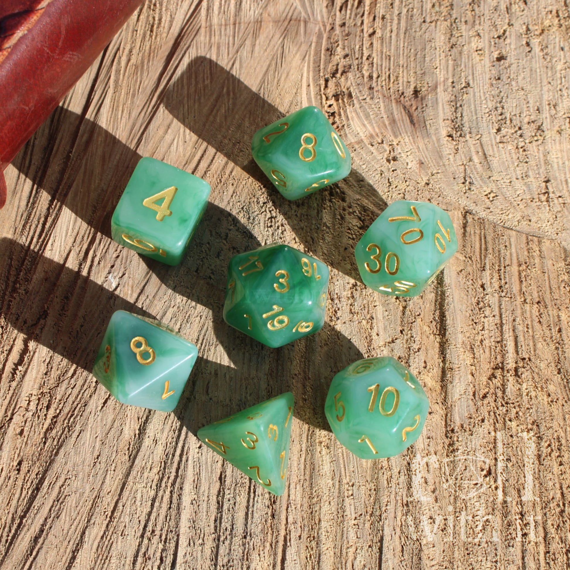 Set of green polyhedral playing dice with gold numbers on a wooden surface