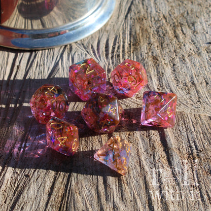 Pink and purple dice set on a wooden surface with a metallic container in the background.