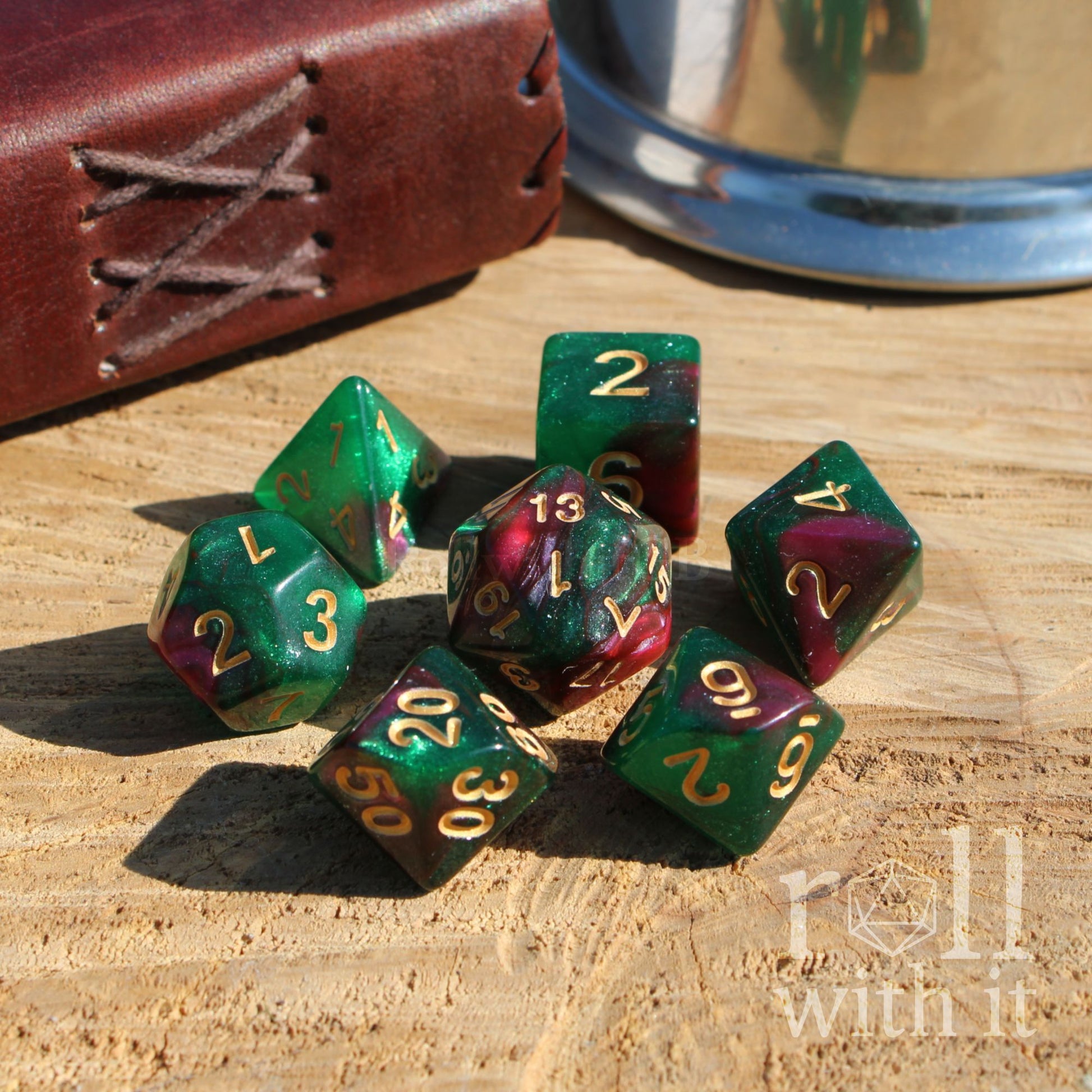 Set of green and purple polyhedral dice with gold numbers on a wooden surface, featuring 'roll with it' branding.