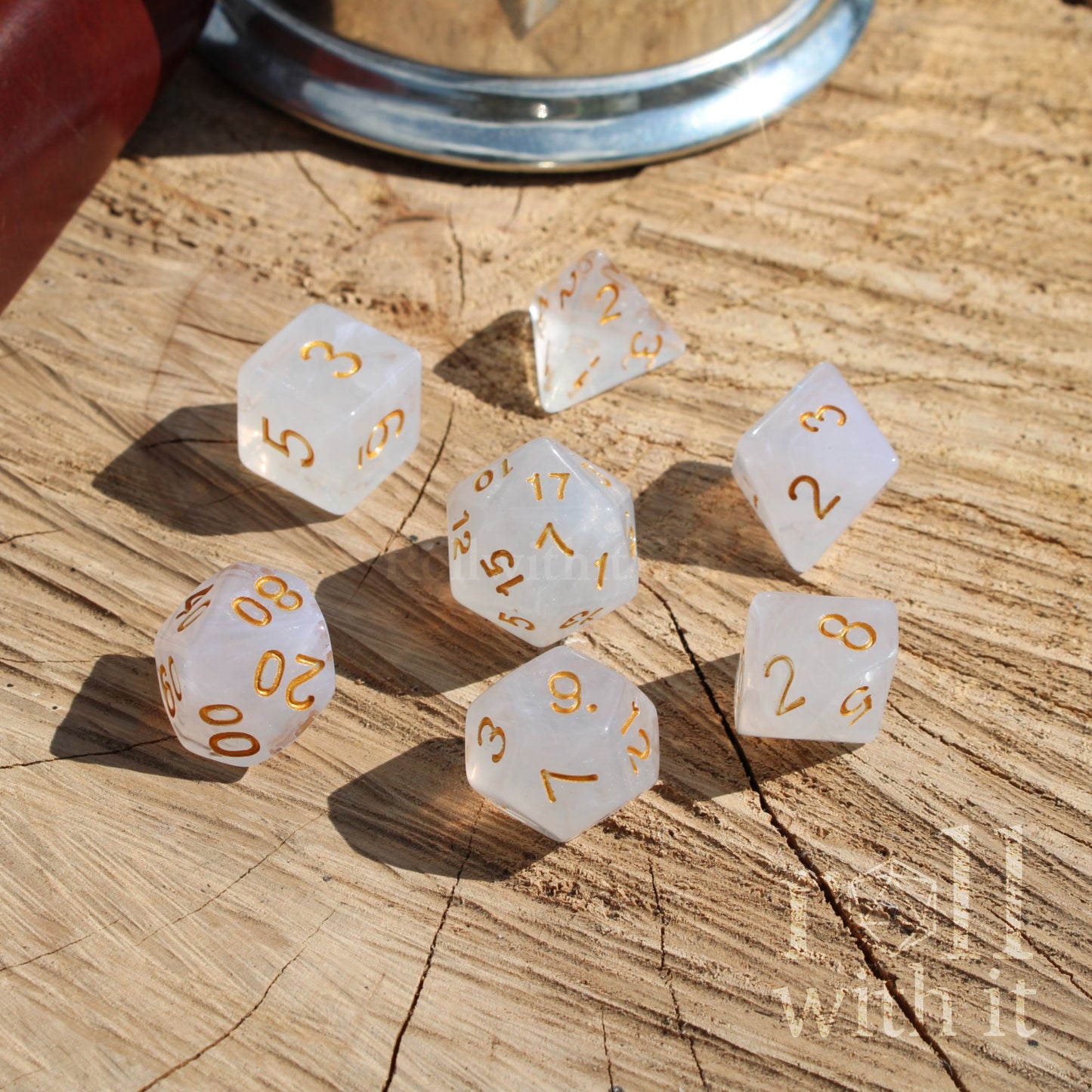 Set of 7 white polyhedral D&D dice with gold numbers on a wooden surface