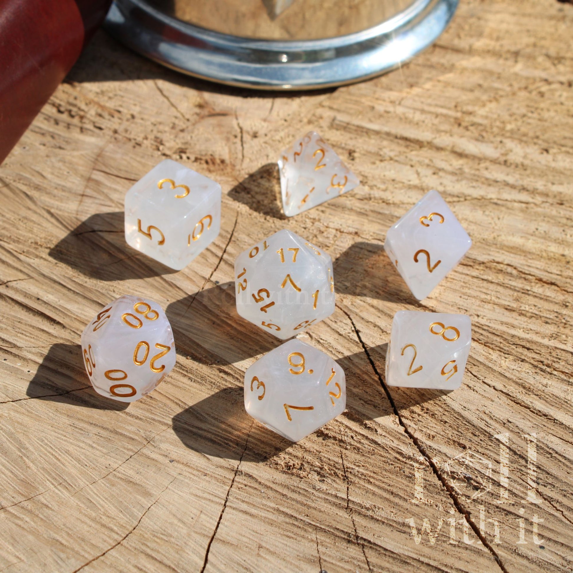 Set of 7 white polyhedral D&D dice with gold numbers on a wooden surface