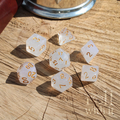 Set of 7 white polyhedral D&D dice with gold numbers on a wooden surface