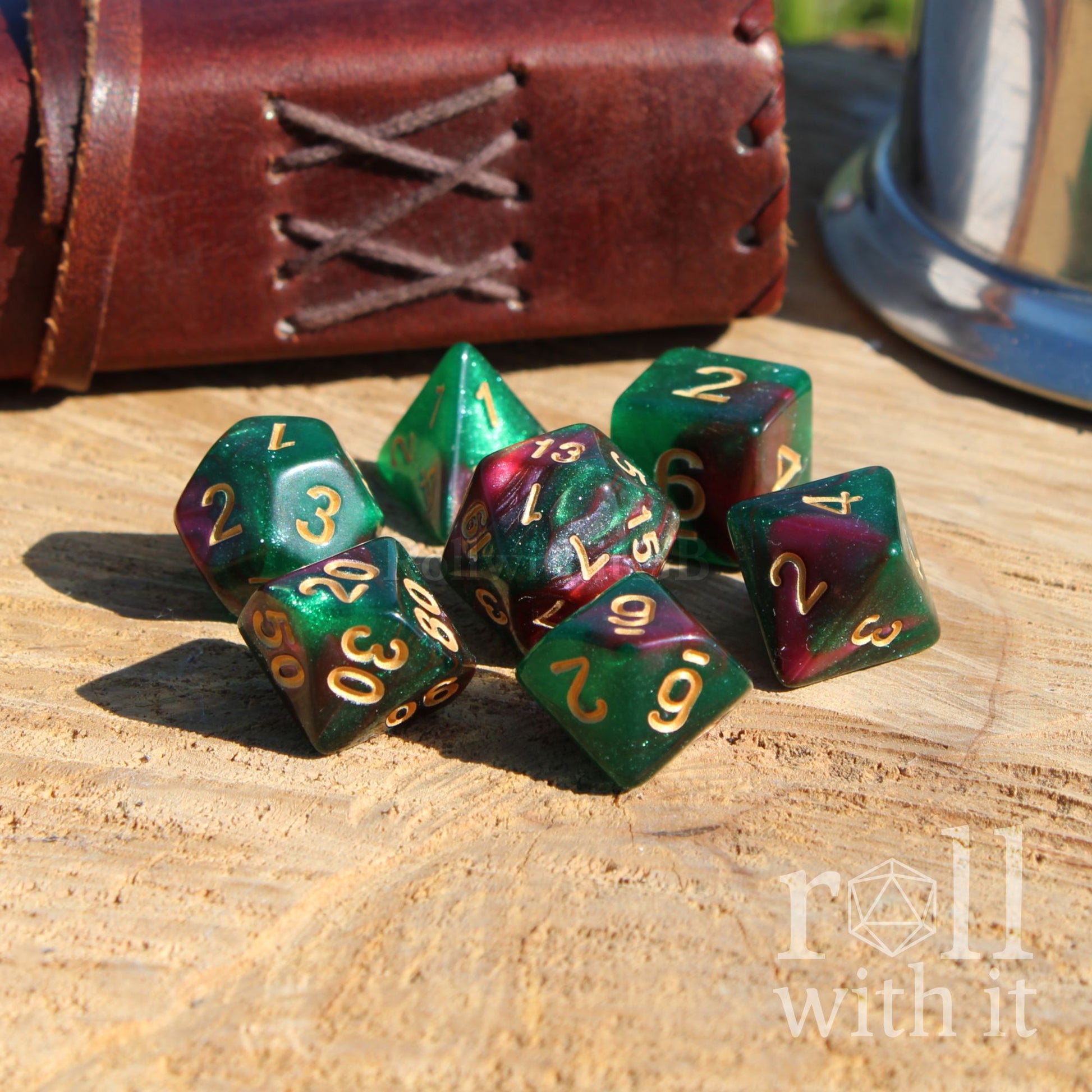 Set of green glittery purple polyhedral dice with gold numbers on a wooden surface, with 'roll with it' logo.