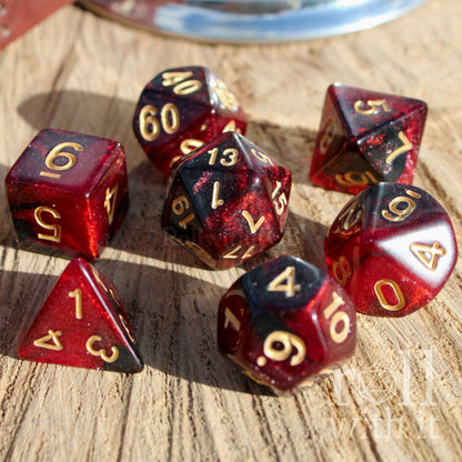 Set of red and black polyhedral starry glitter filled dice with gold numbers on a wooden surface
