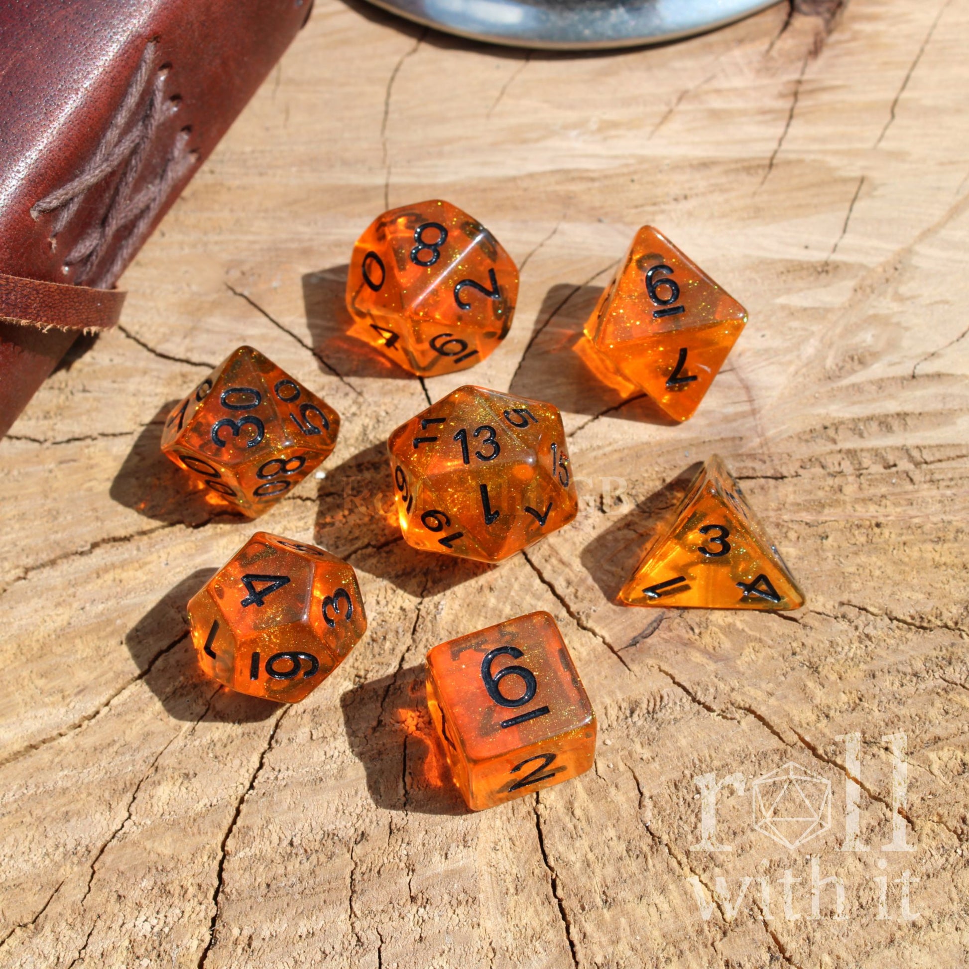Set of bright shiny orange dice with black numbers and yellow glitter on a wooden surface