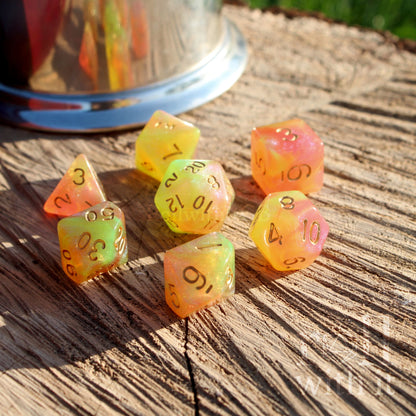 Set of colorful and bright pink green yellow glitter filled polyhedral dice on a wooden surface with a metallic cup in the background.