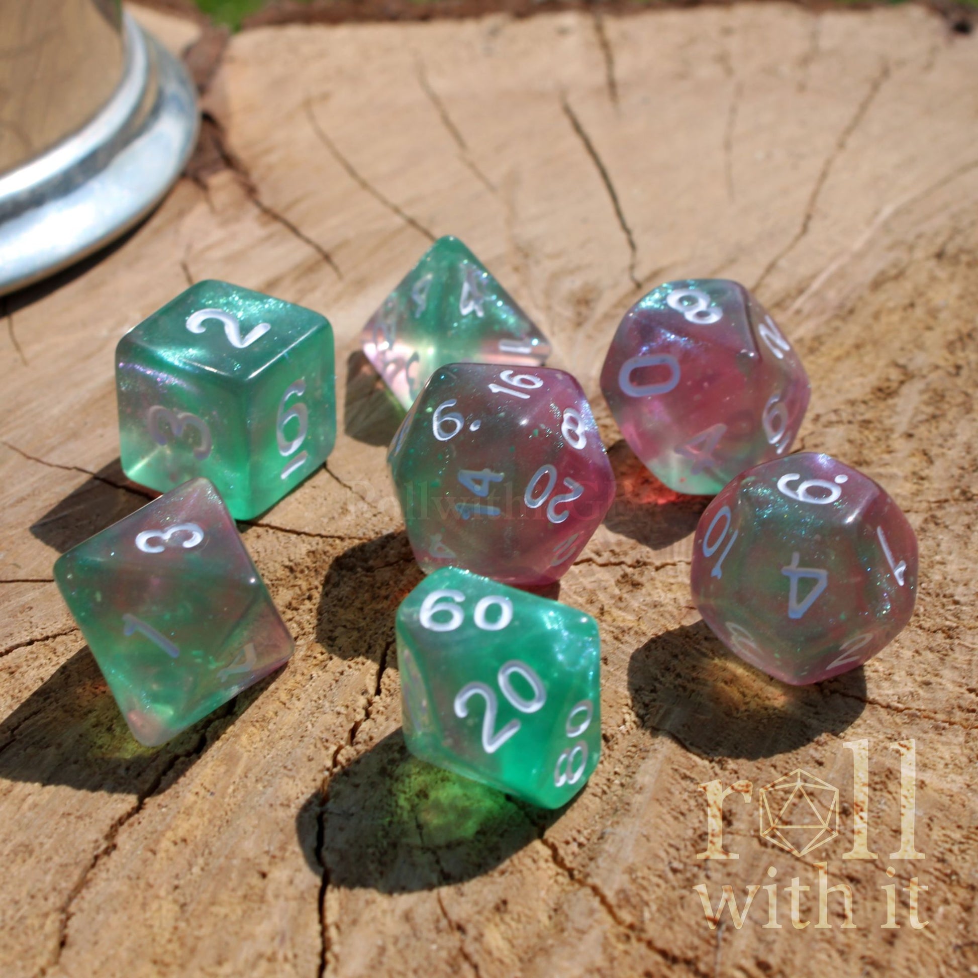 Set of colorful green pink glitter filled glow in the dark polyhedral dice on a wooden surface with 'roll with it' branding.