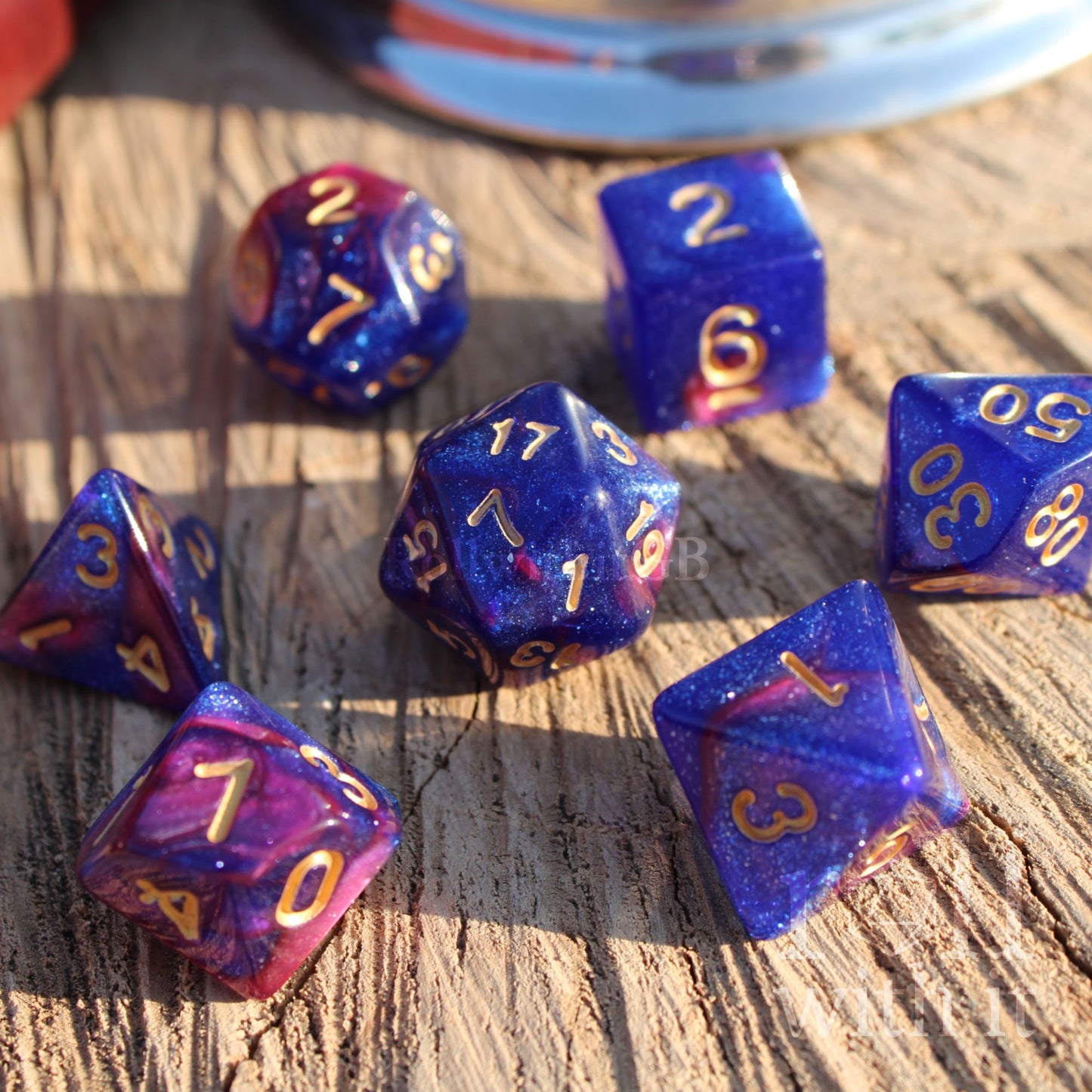 Set of blue and purple RPG polyhedral dice with gold numbers on a wooden surface.