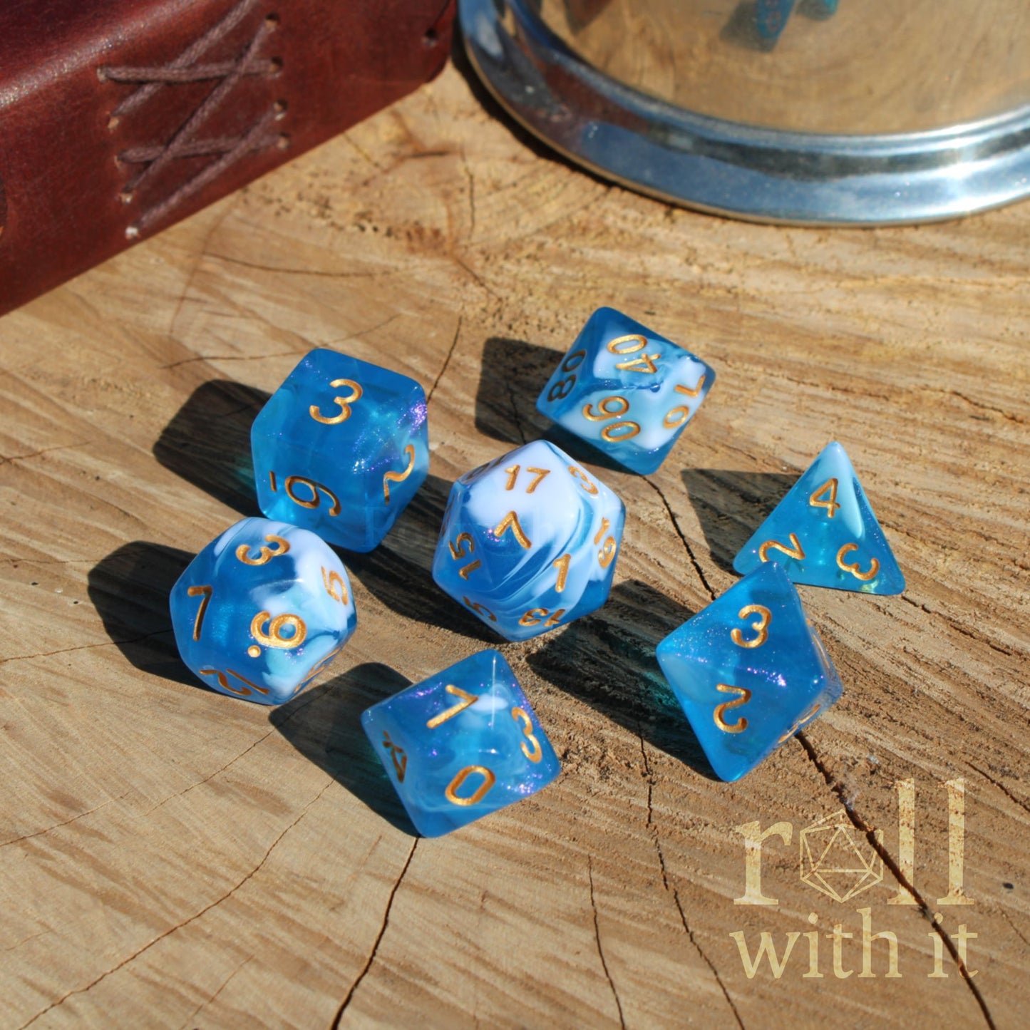 Blue glittery polyhedral dice set on a wooden surface with 'roll with it' text.