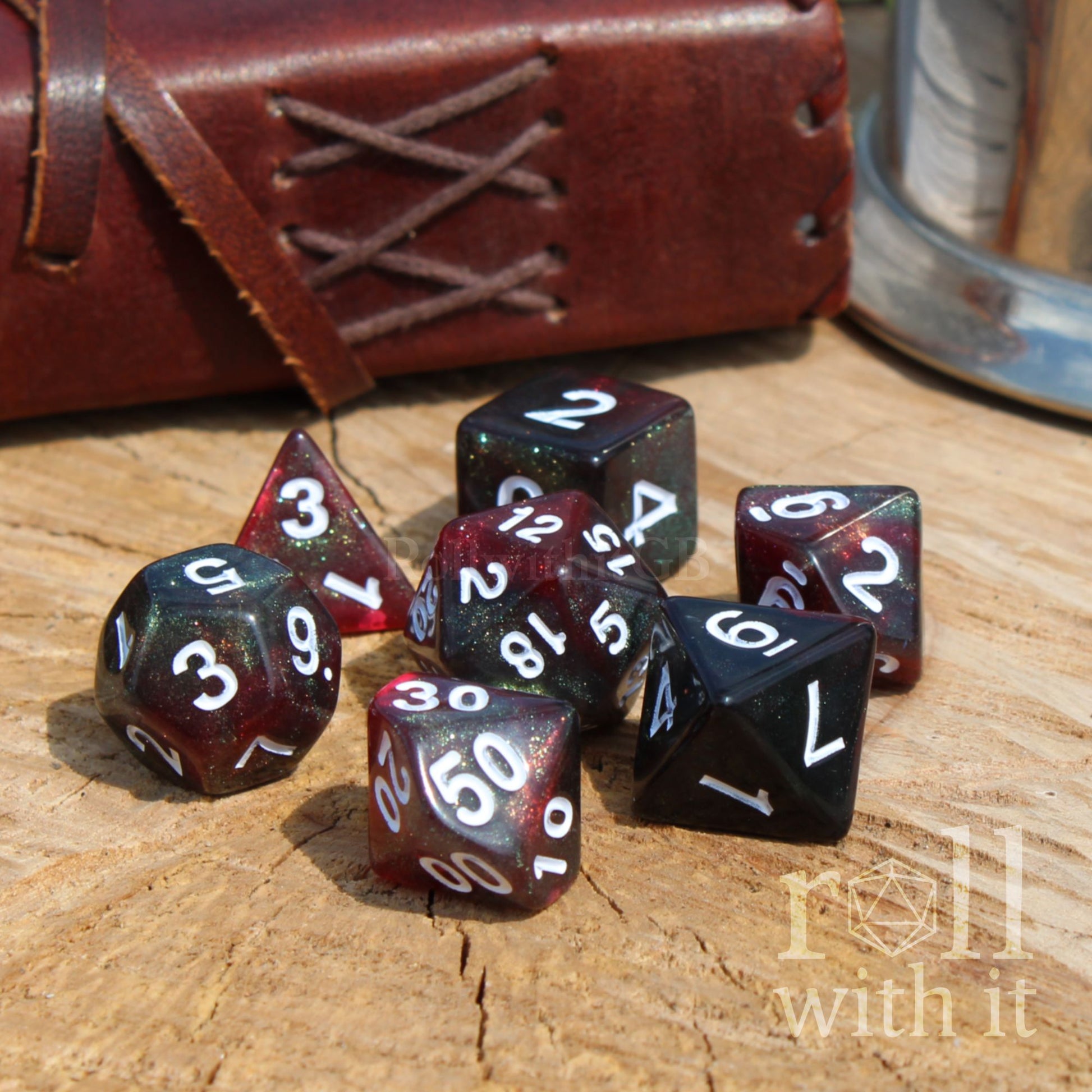 Set of red black green glitter polyhedral dice on a wooden surface with a leather-bound book and metal canister in the background.