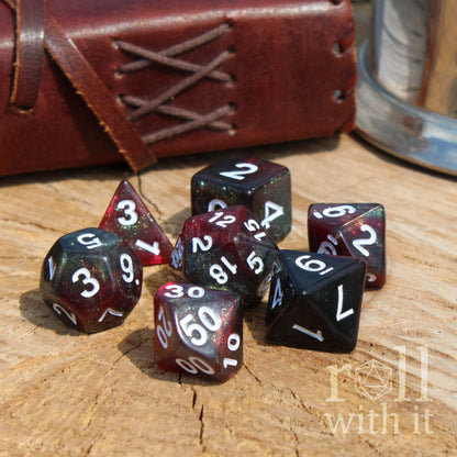 Set of red black green glitter polyhedral dice on a wooden surface with a leather-bound book and metal canister in the background.