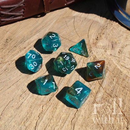 Set of 7 teal and copper red glow in the dark polyhedral luxury playing dice on a wooden surface with 'roll with it' text.