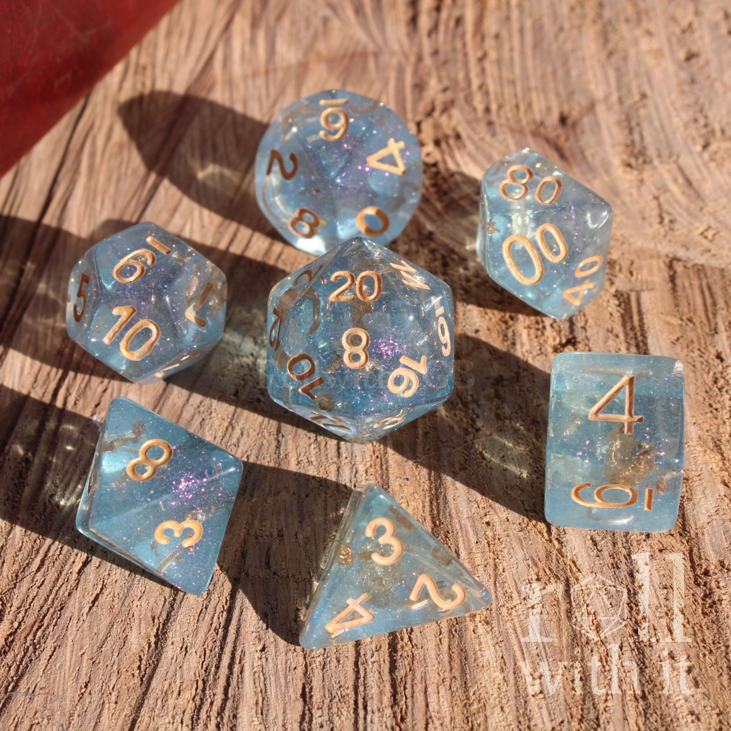 Set of pale blue gold foil filled clear polyhedral dice with gold numbers on a wooden surface
