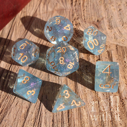 Set of pale blue gold foil filled clear polyhedral dice with gold numbers on a wooden surface