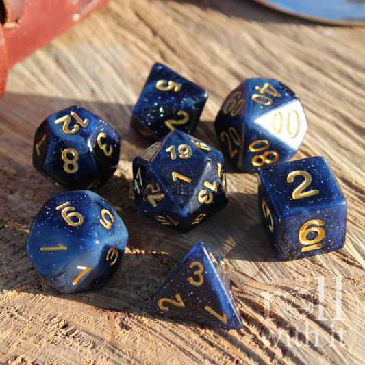 Blue starry glitter midnight sky themed polyhedral dice set with gold numbers on a wooden surface