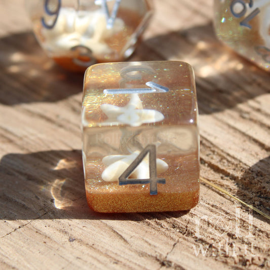 Translucent dice with a starfish lying ontop of golden glitter sand on a wooden surface