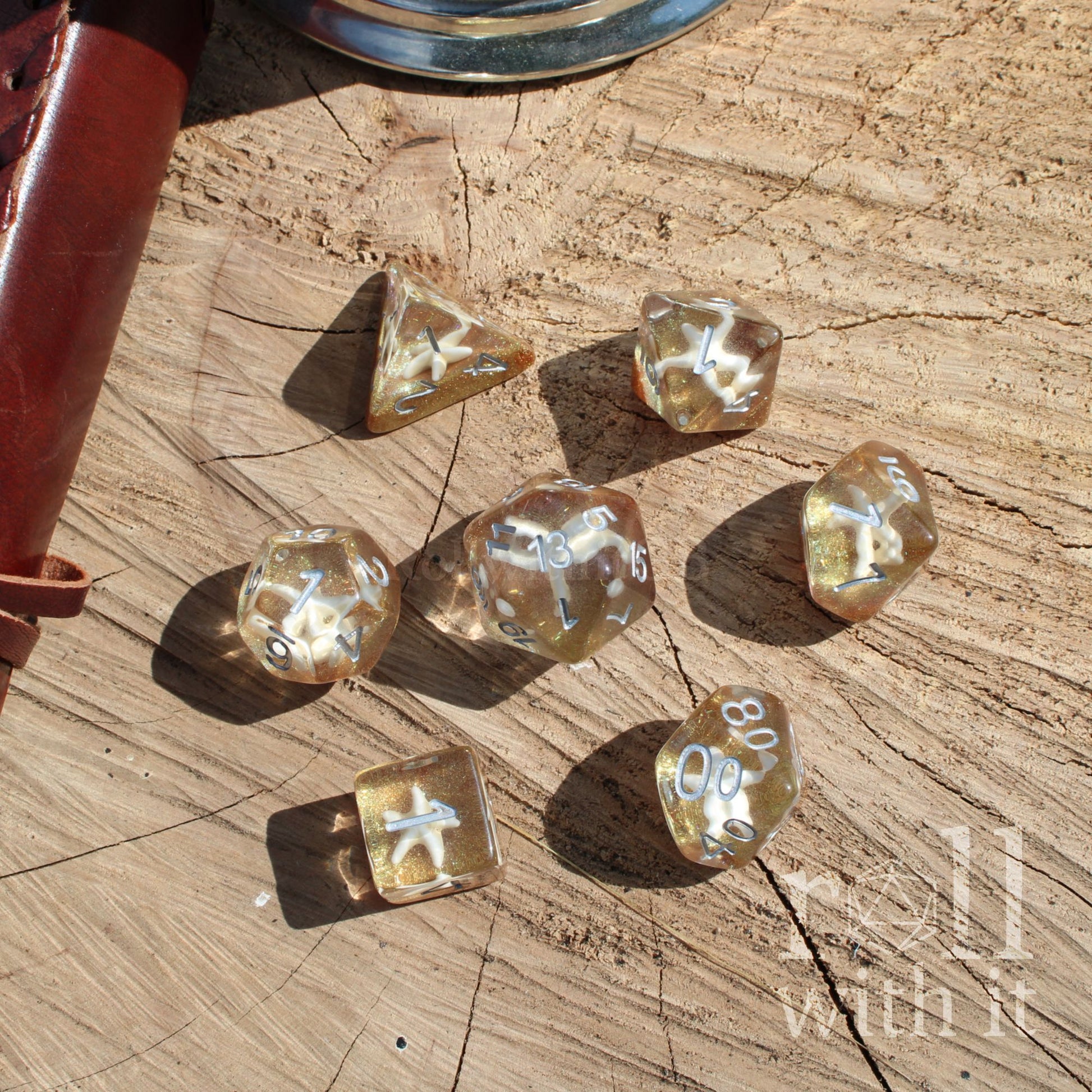 Set of gold polyhedral dice on a wooden surface with 'with it' branding.