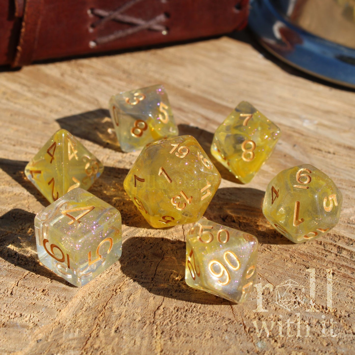 Set of yellow and grey mixed glitter filled polyhedral dice with gold numbers on a wooden surface, featuring the brand 'roll with it'.
