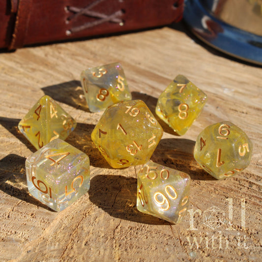 Set of yellow and grey mixed glitter filled polyhedral dice with gold numbers on a wooden surface, featuring the brand 'roll with it'.