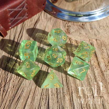 Set of green glittery clear polyhedral dice with gold numbers on a wooden surface, with 'roll with it' branding.