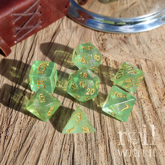 Set of green glittery clear polyhedral dice with gold numbers on a wooden surface, with 'roll with it' branding.