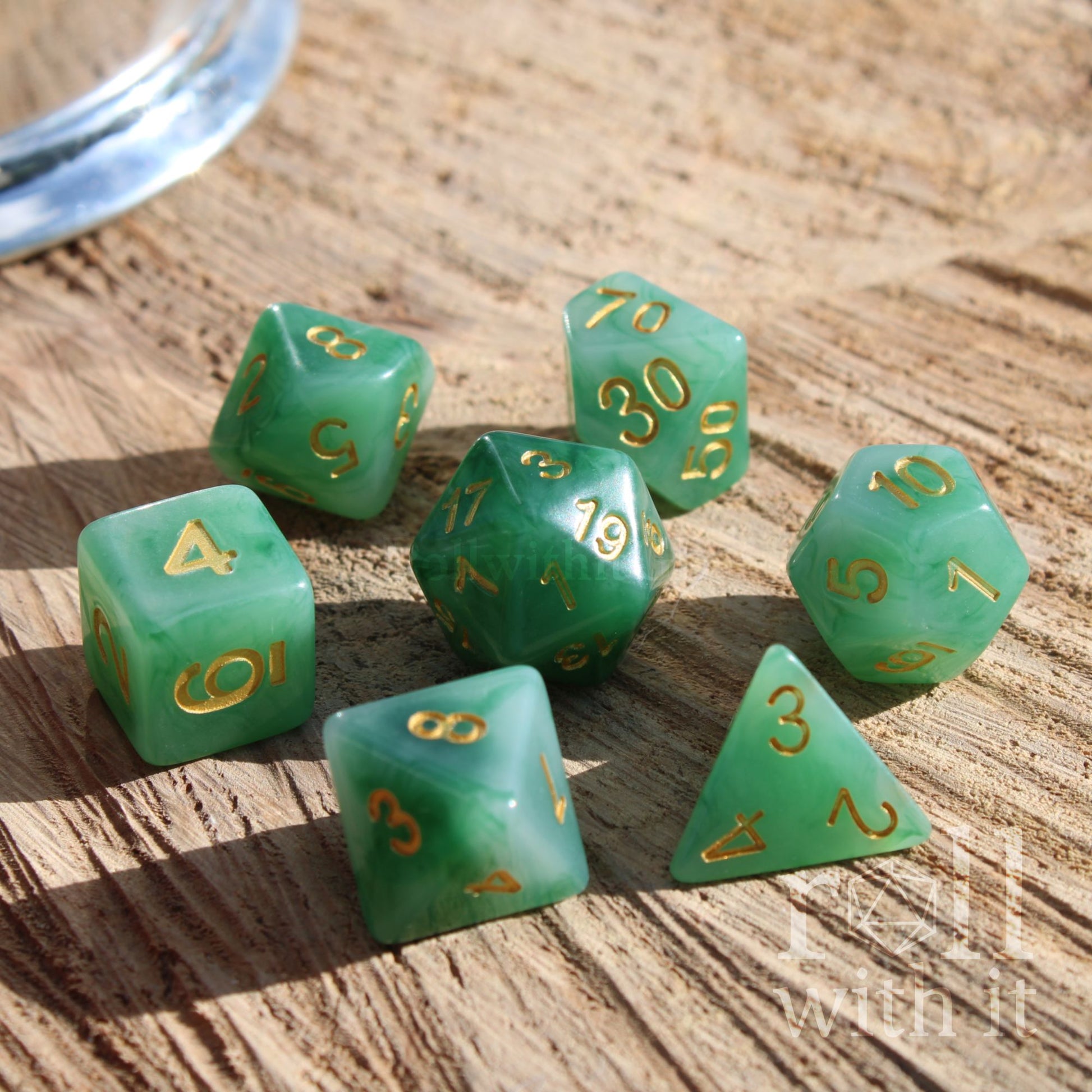 Set of green milky wispy resin polyhedral dice with gold numbers on a wooden surface