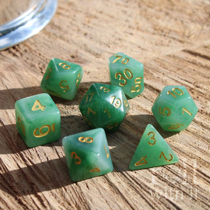 Set of green milky wispy resin polyhedral dice with gold numbers on a wooden surface