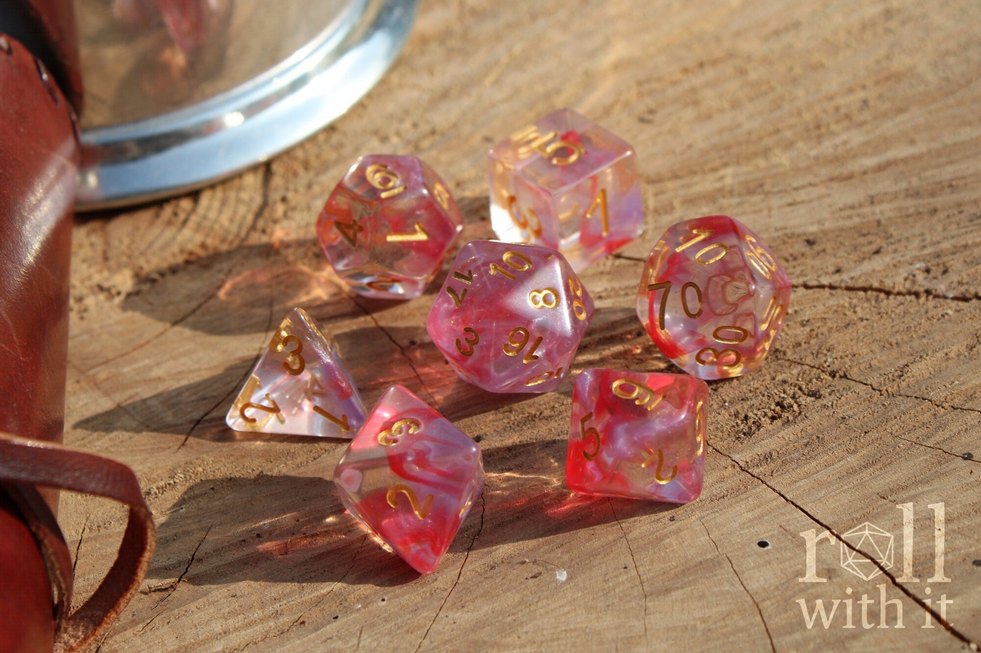 Set of translucent rose pink and purple clear roleplaying dice with gold numbers on a wooden surface