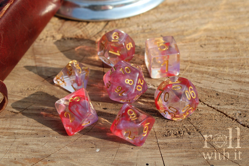 Set of translucent rose pink and purple clear roleplaying dice with gold numbers on a wooden surface