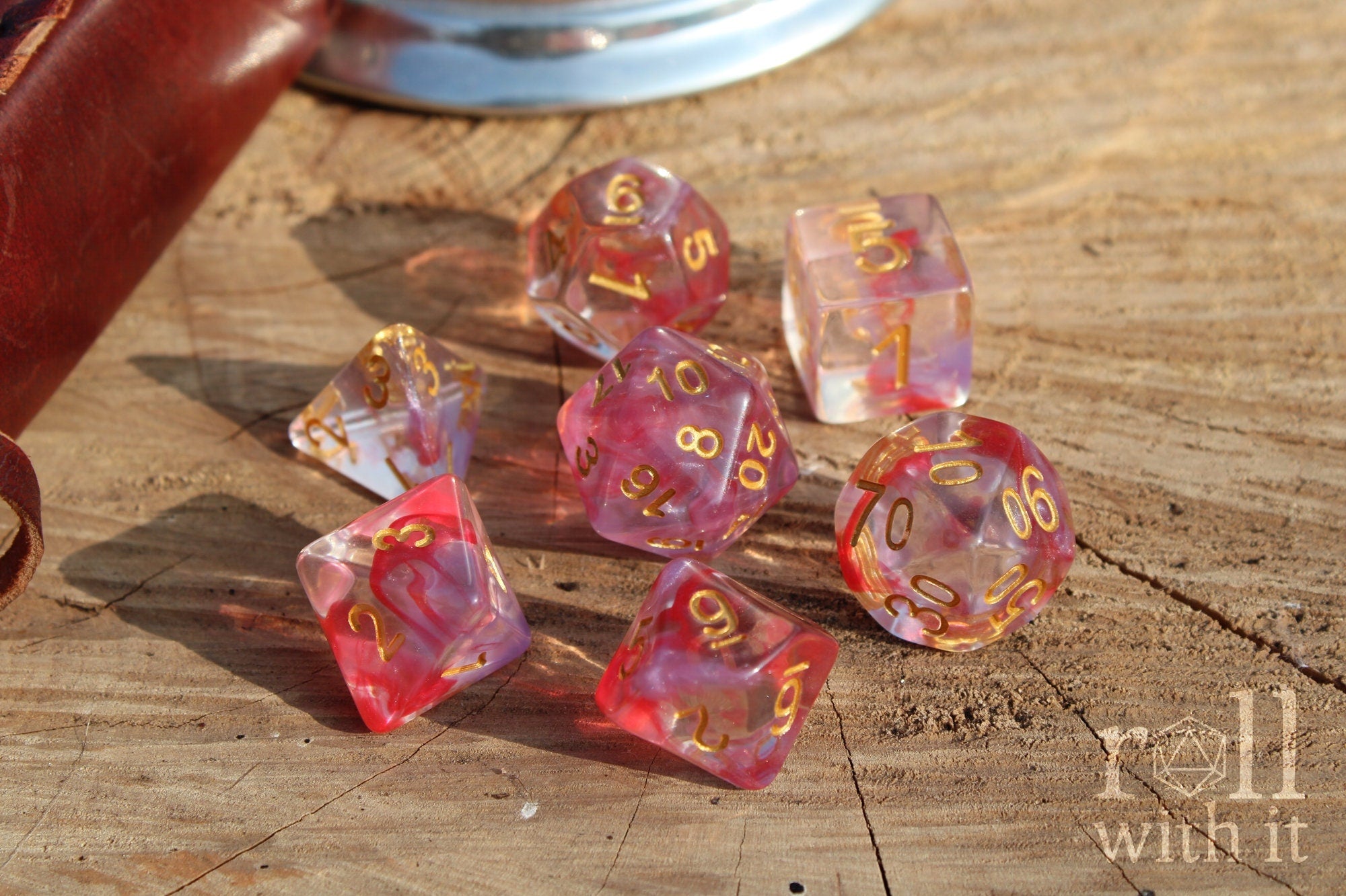 Set of translucent rose pink and purple clear roleplaying dice with gold numbers on a wooden surface