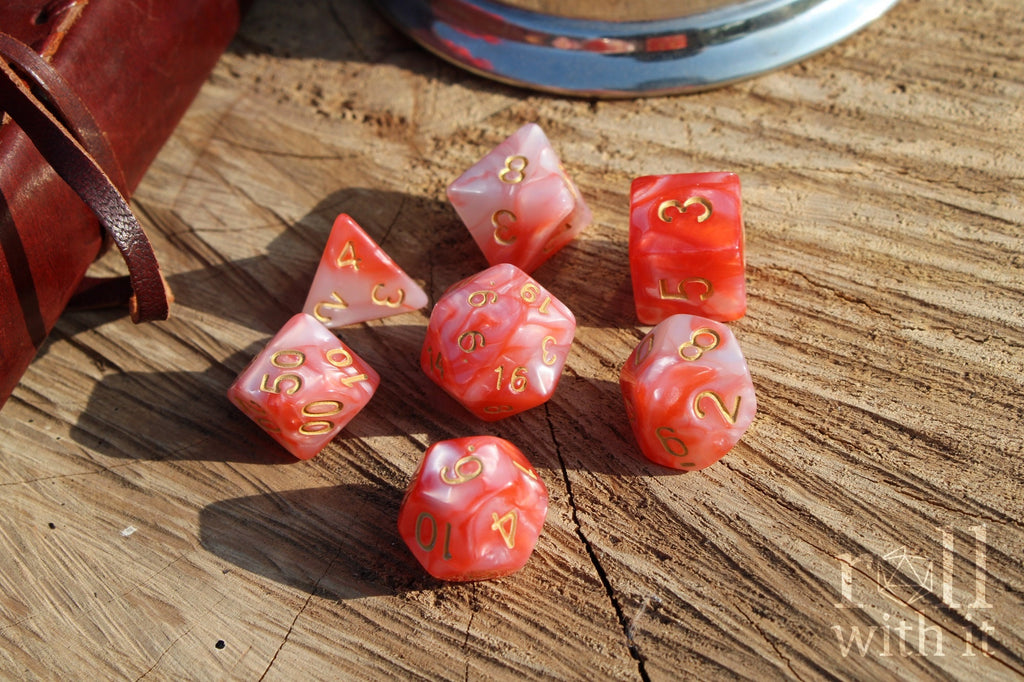 Set of shiny pink and lobster red polyhedral dice with gold numbers on a wooden surface
