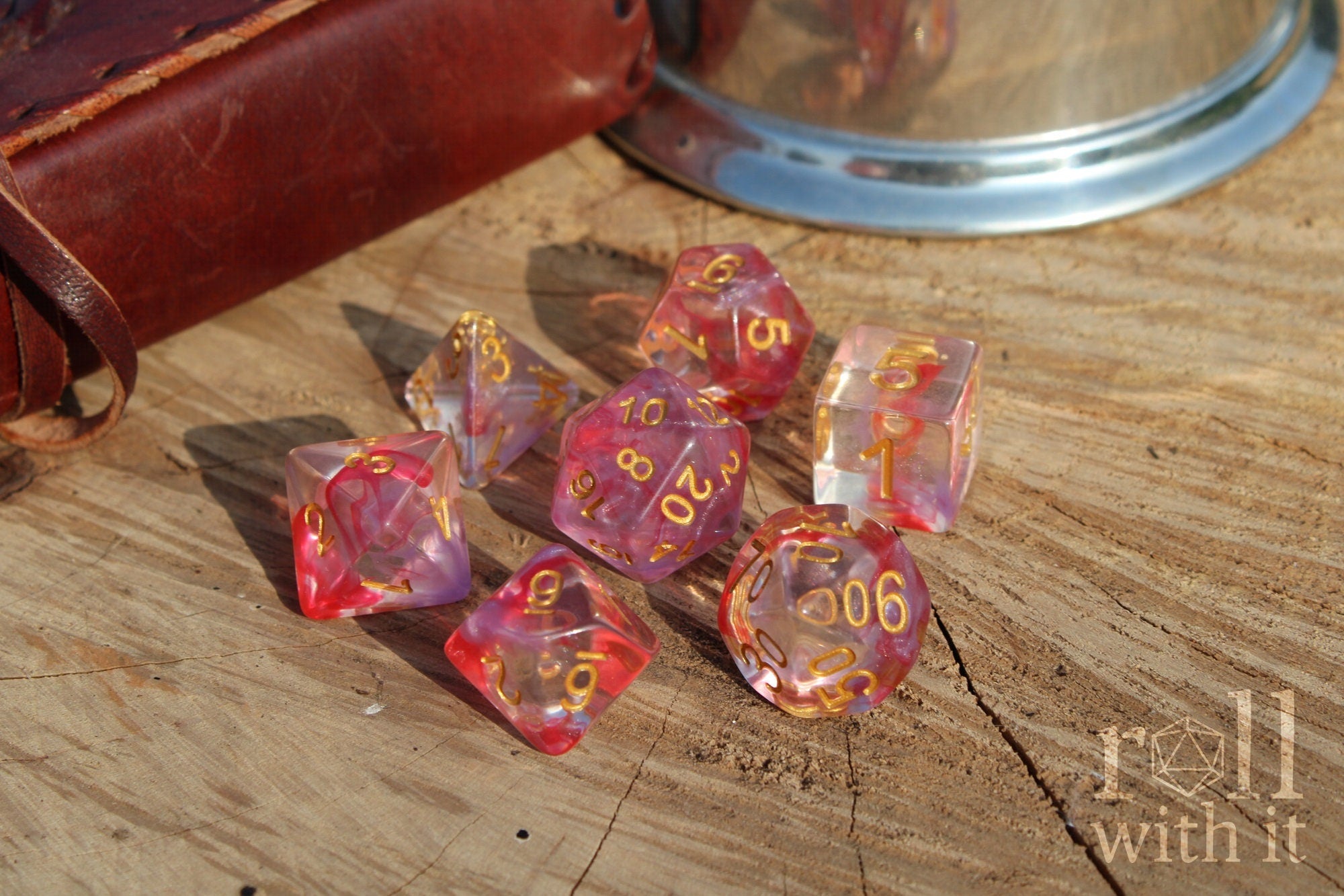 Set of rose pink and purple clear role playing DND dice with gold numbers on a wooden surface