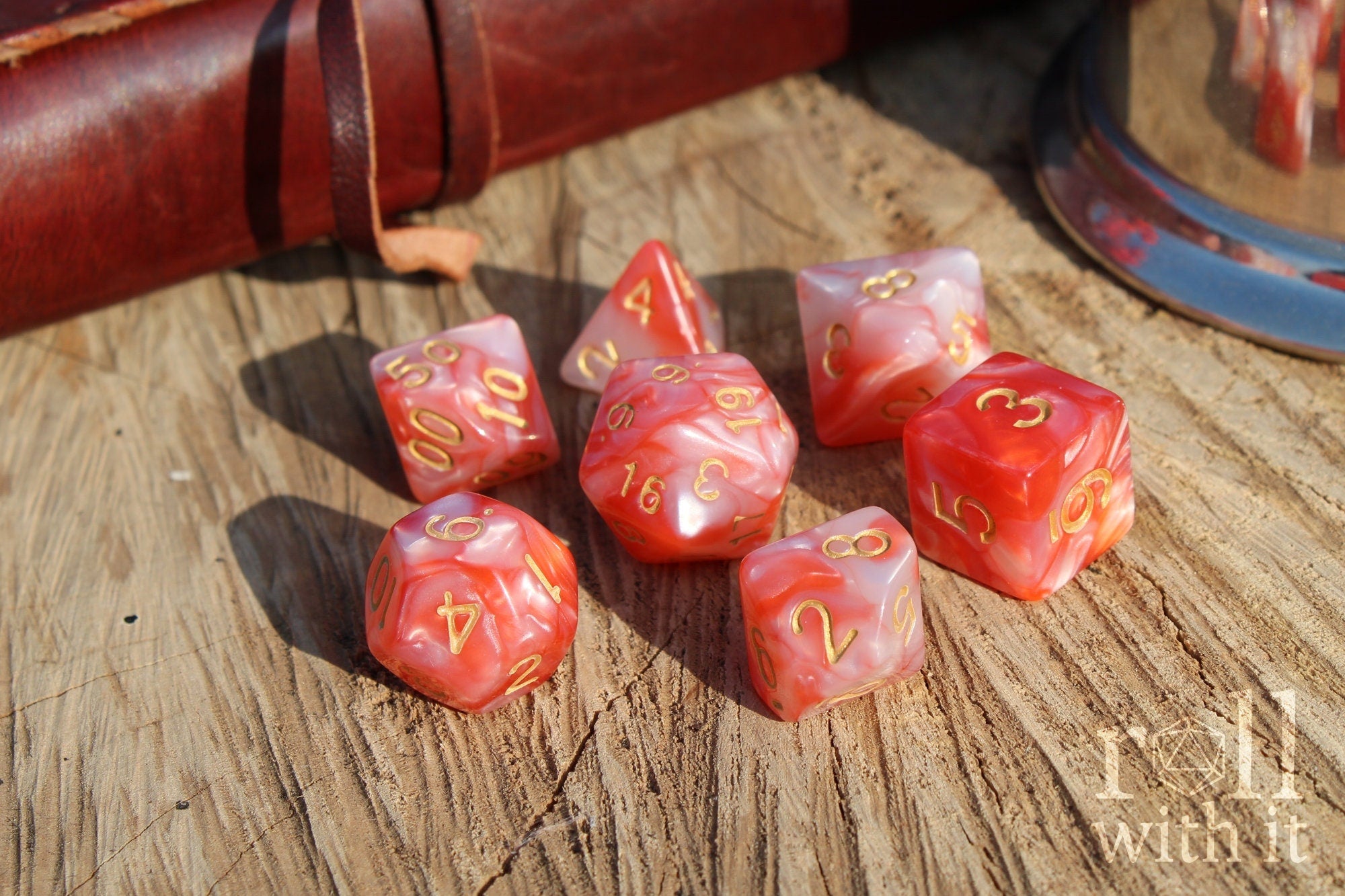 Set of shiny pink and lobster red polyhedral dice with gold numbers on a wooden surface