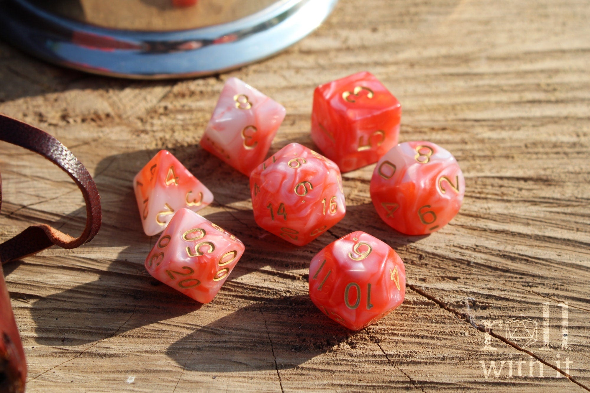 Set of shiny pink and lobster red polyhedral dice with gold numbers on a wooden surface