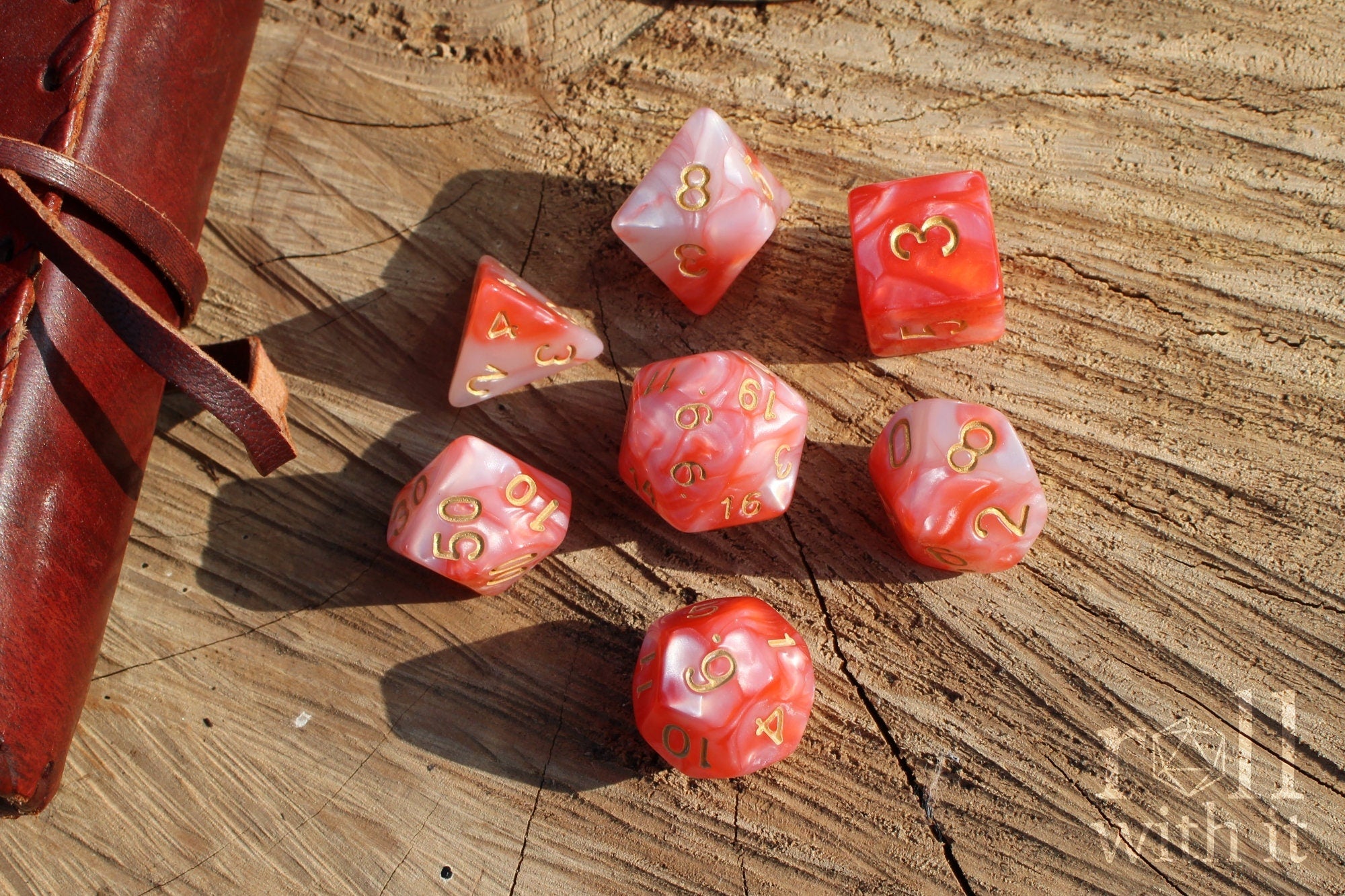 Set of shiny pink and lobster red polyhedral dice with gold numbers on a wooden surface