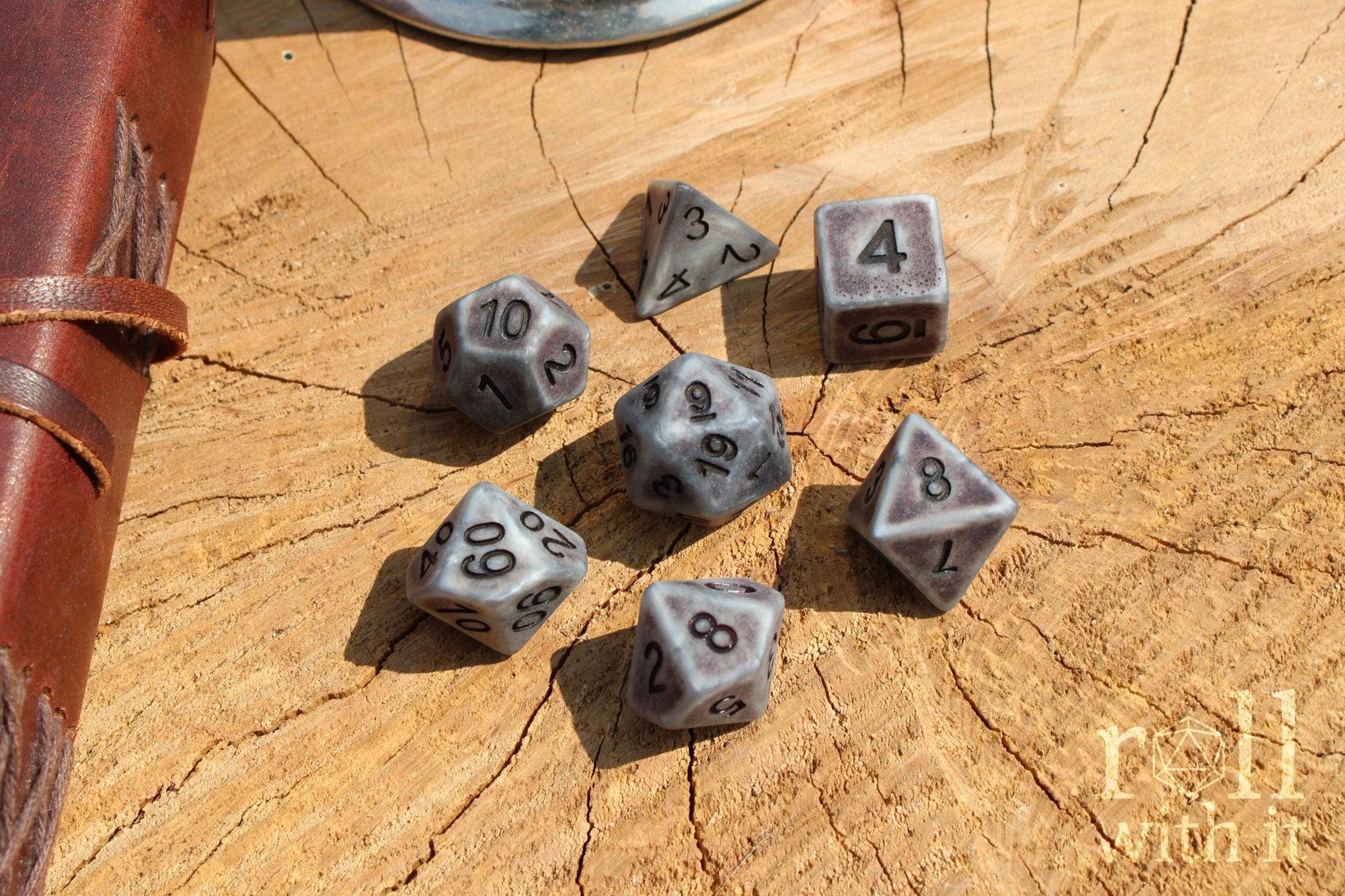 Set of matte industrial style polyhedral roleplaying dice with pink numbers sat on a wooden surface