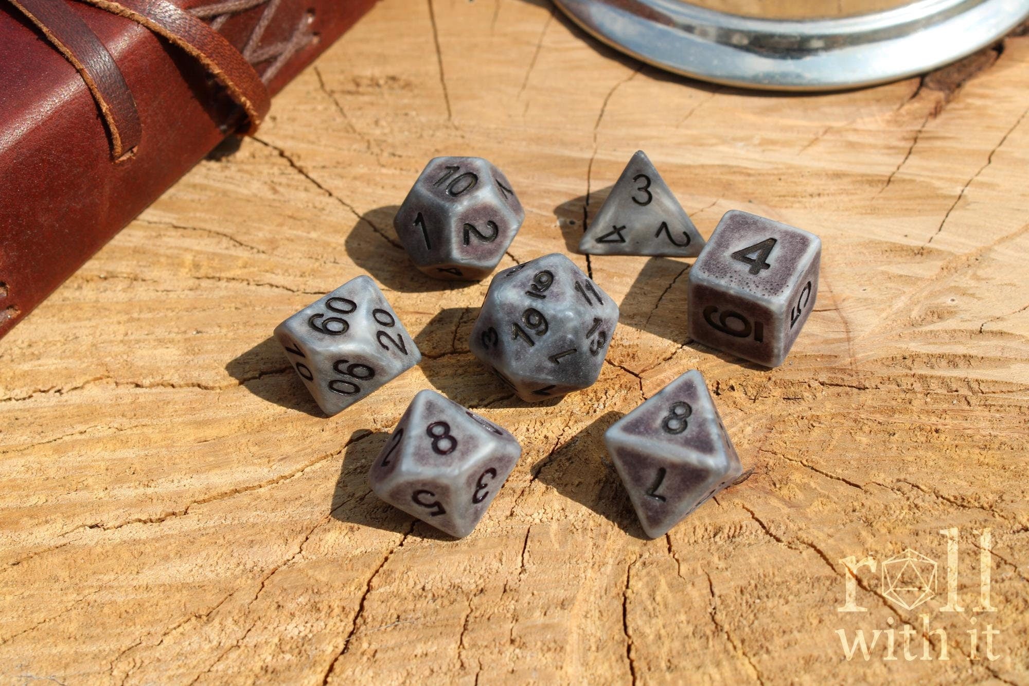 Set of stone-like matte silver polyhedral RPG dice with black numbers on a wooden surface