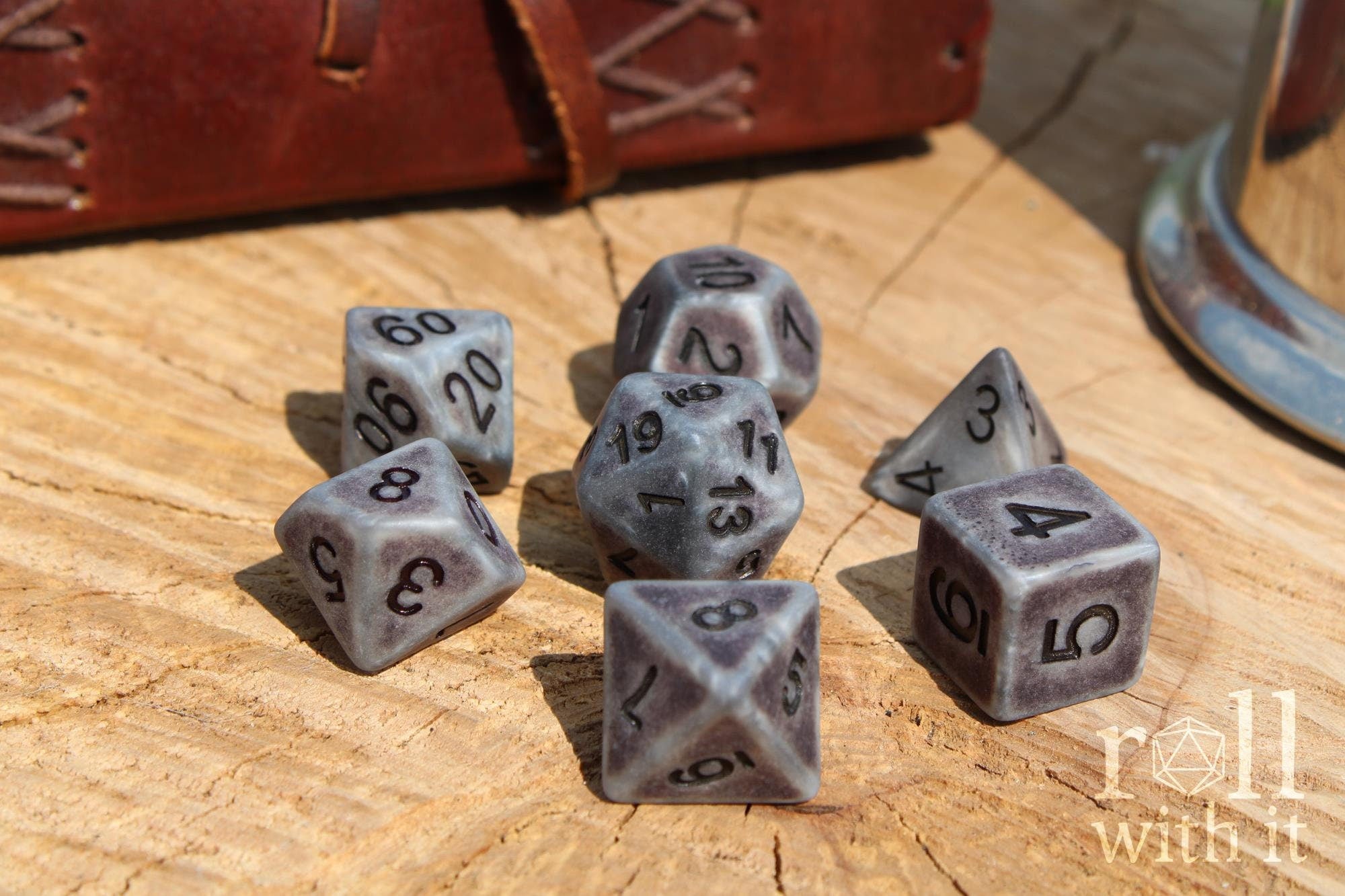 Set of concrete looking matte silver polyhedral DND dice with black numbers on a wooden surface