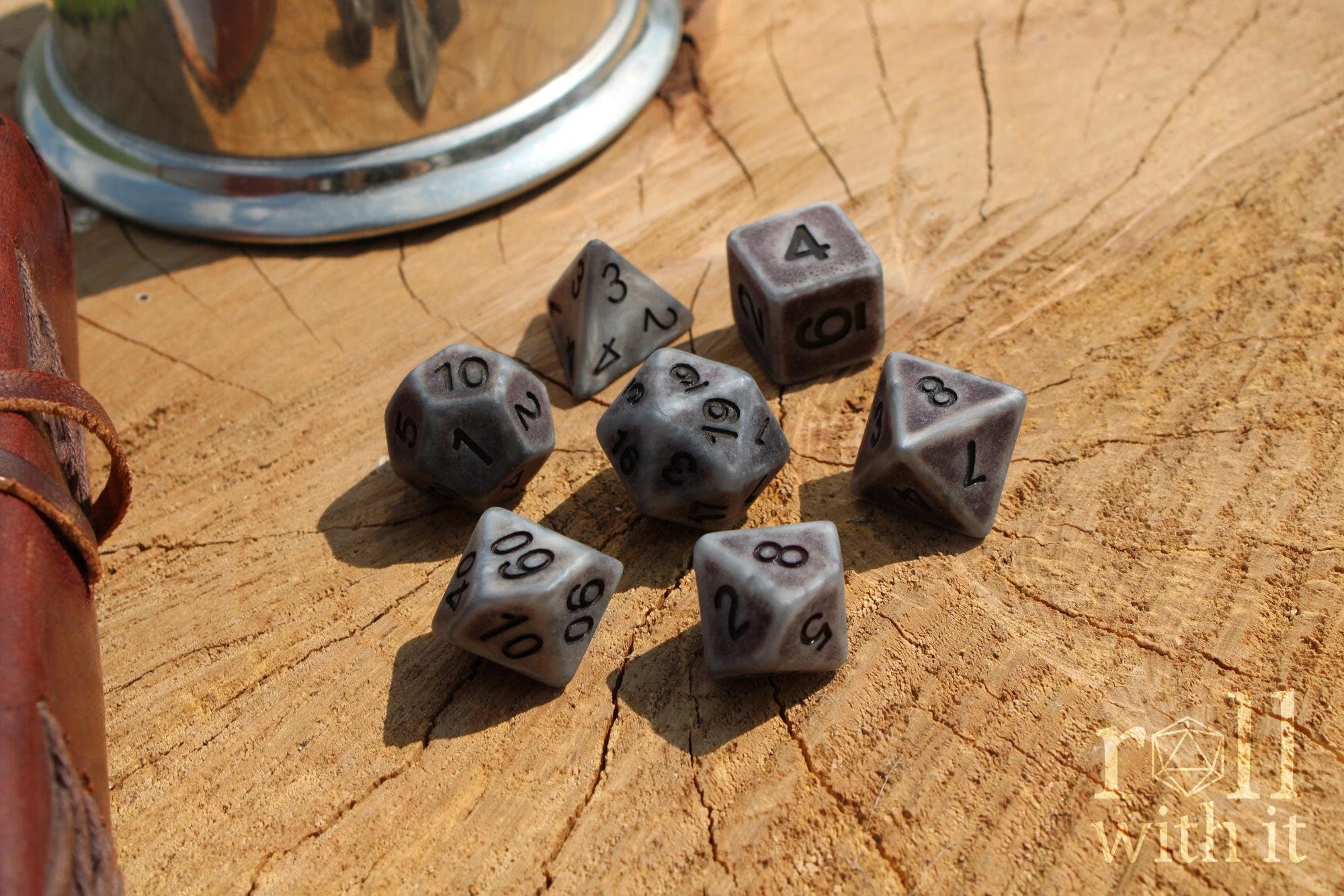 Set of matte silver polyhedral dice with black numbers on a wooden surface