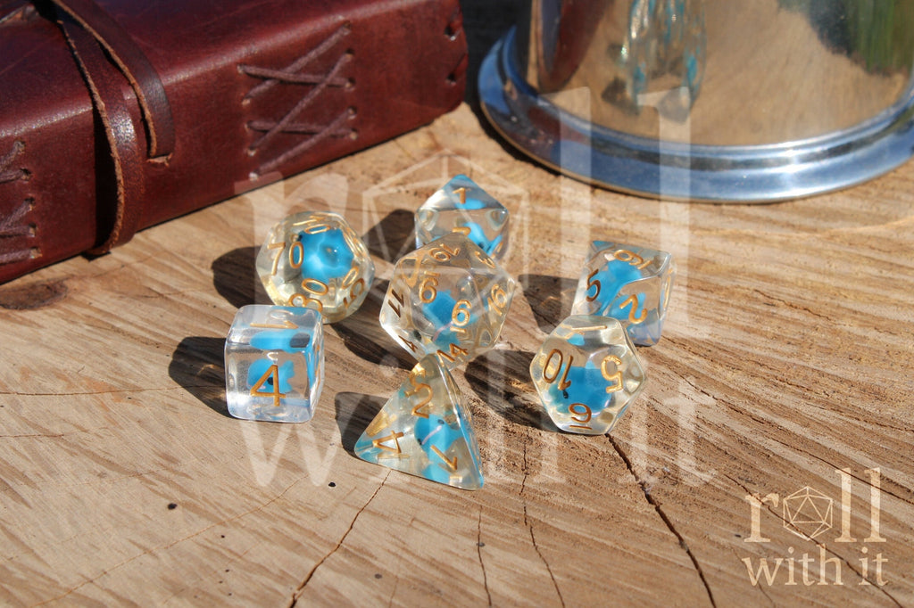 Set of clear polyhedral role playing dice with a small blue whale inside, with gold numbering on a wooden surface