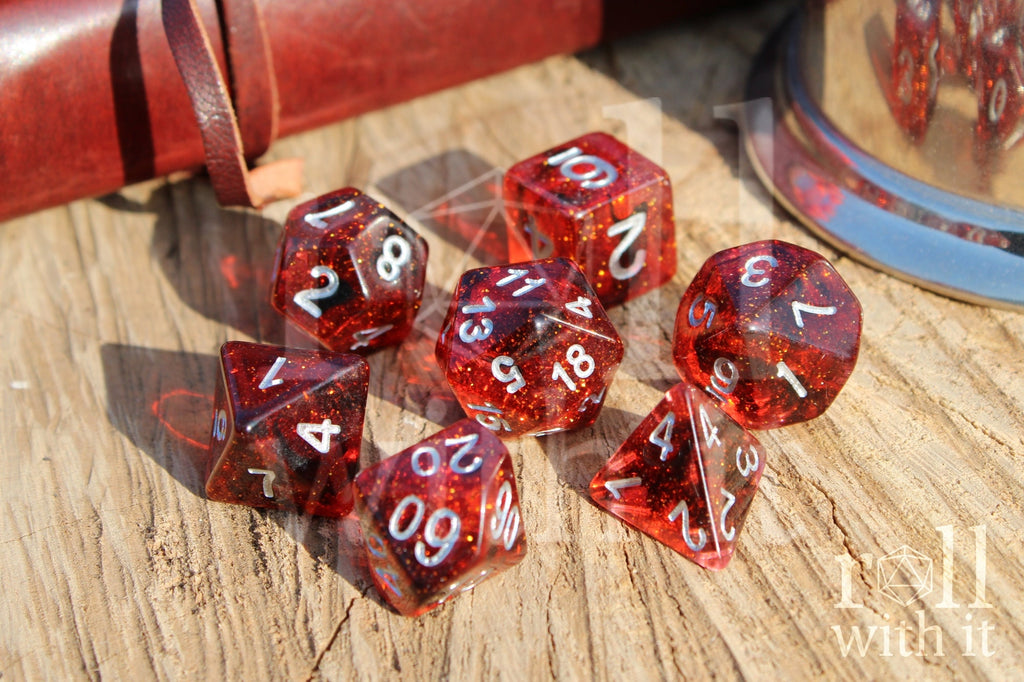 Set of red and black glittery polyhedral DnD roleplaying dice with silver numbers on a wooden surface