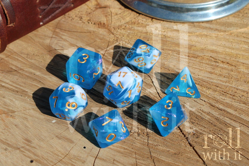 Set of blue and white glittery polyhedral dice with gold numbers on a wooden surface
