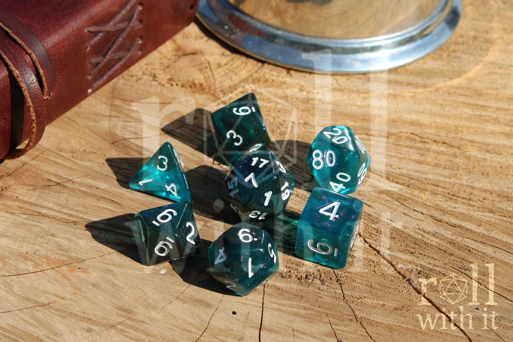 Set of 7 teal and black polyhedral roleplaying dice with flecks of lilac glitter on a wooden surface