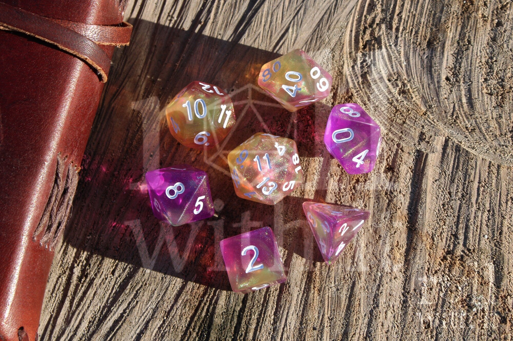 Set of colourful purple pink and yellow glittery polyhedral DnD dice on a wooden surface